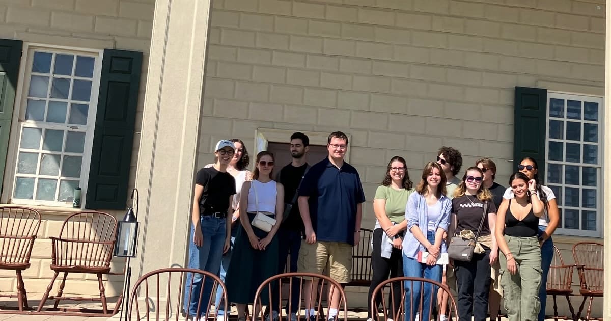 Tour group on the porch of Mount Vernon, with authentic period chairs and painted brick.