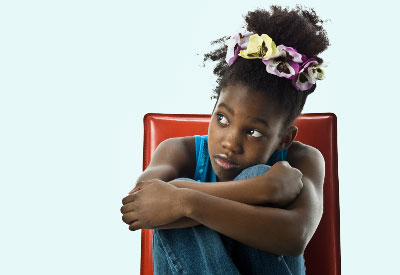 Child sits in chair hugging her knees