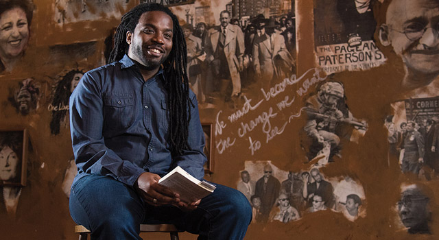 Man sits on stool onstage, a book on his lap