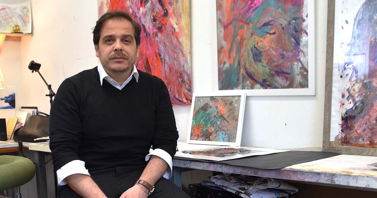 Andres Izquierdo seated in front of his paintings in his studio