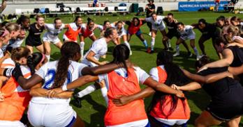 AU women soccer team huddled together, Brooke Steel in center, shouting.