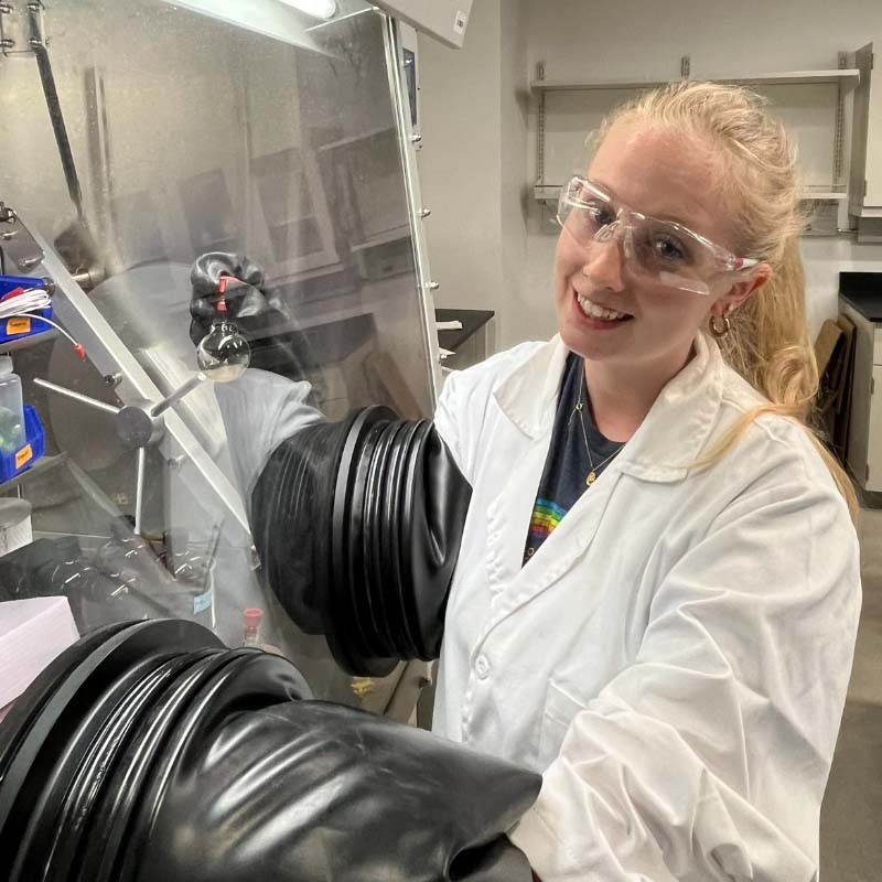 Kelsey Kirsch, working in lab glovebox, synthesizing a compound.