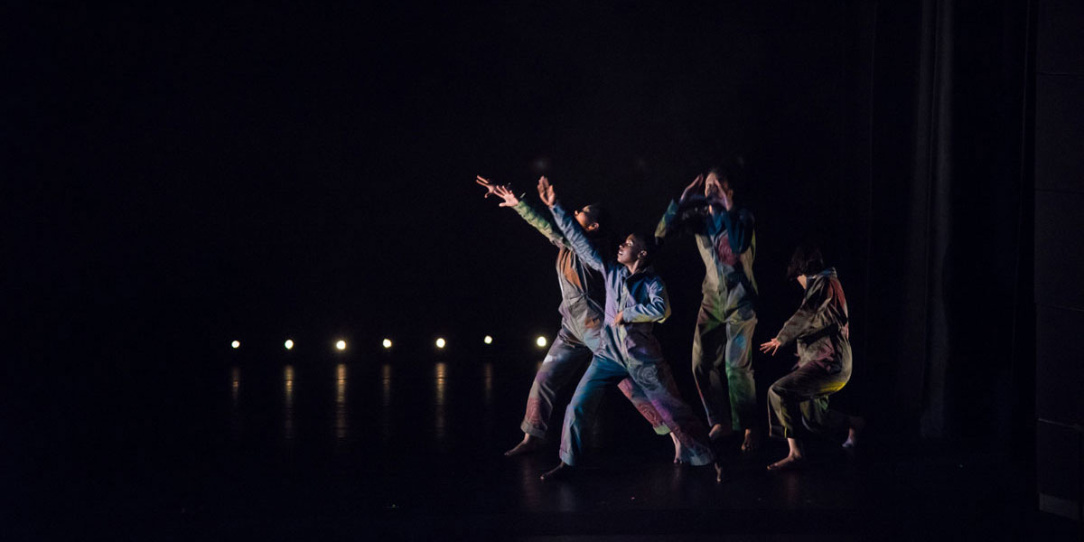 A group of children on a dark stage reach for the sky