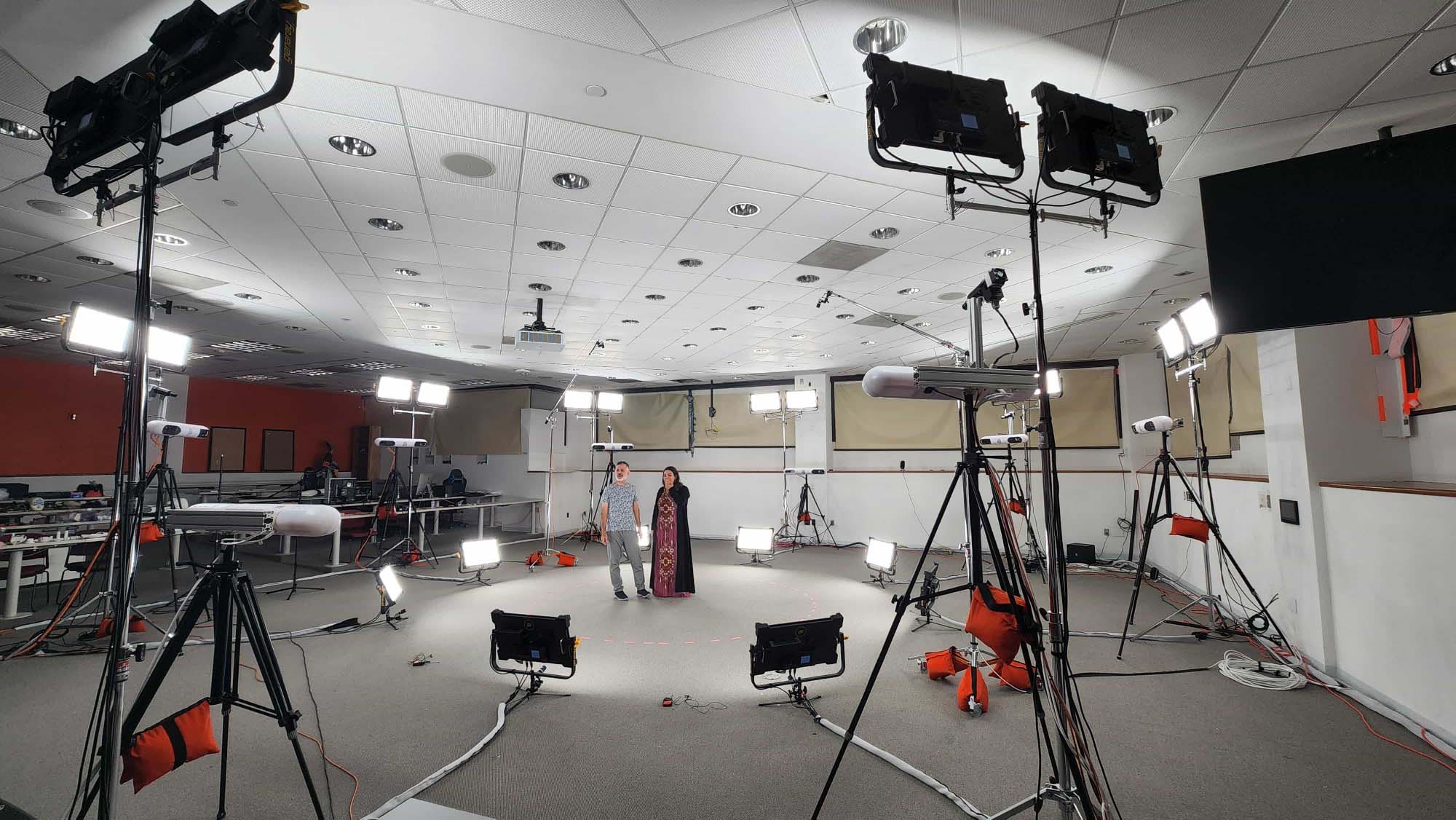 A bearded man in modern dress and a woman in traditional Emirati dress stand at the center of a volumetric capture studio stage