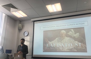 A man stands in front of a projector screen with an image of Pope Francis