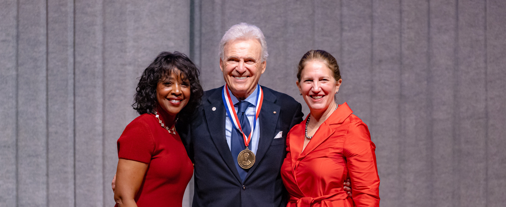 (left to right) AU Board of Trustees chair Gina Adams, Ambassador Stuart Bernstein, and AU President Sylvia M. Burwell stand together onstage at the 2023 President's Circle Celebration