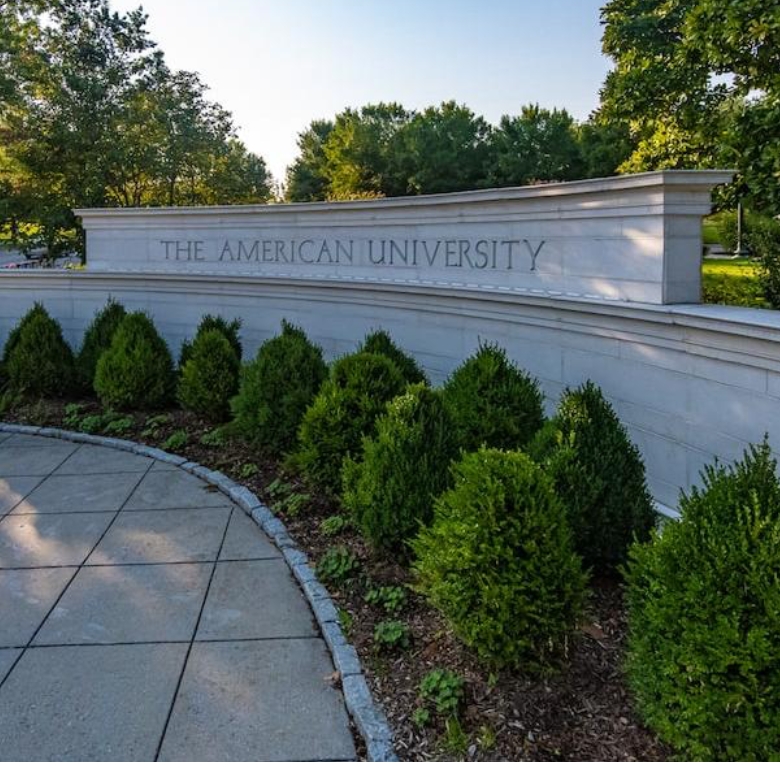 American University entrance with bushes and tress around brick structure with the name of the university