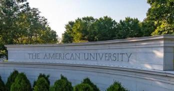 American University entrance with bushes and tress around brick structure with the name of the university