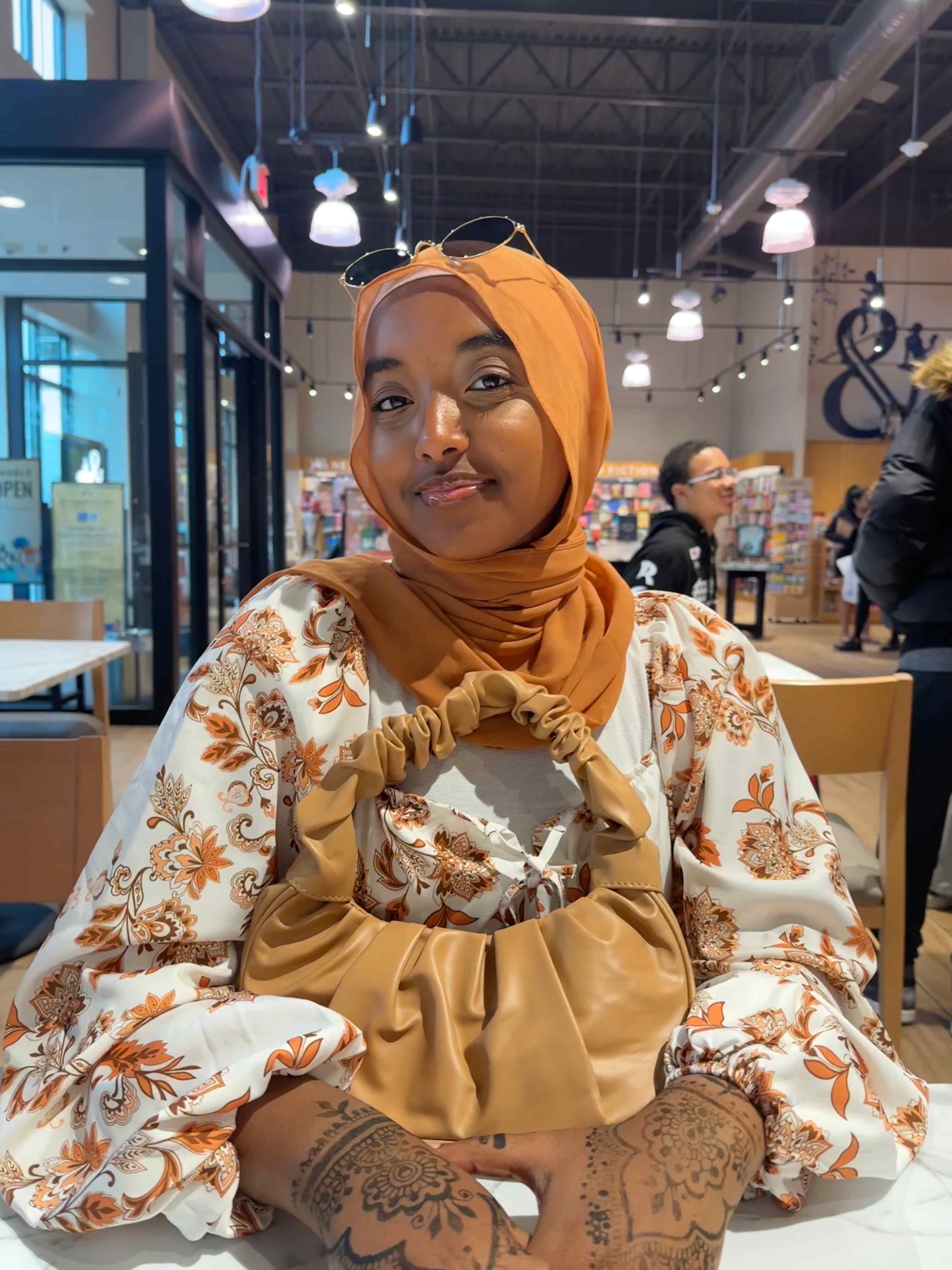 Aseel in an orange headscarfe and a floral shirt sitting at a table