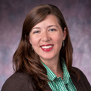 Heashot of Prof Salois with long brown hair, a green plaid shirt and a brown sweater