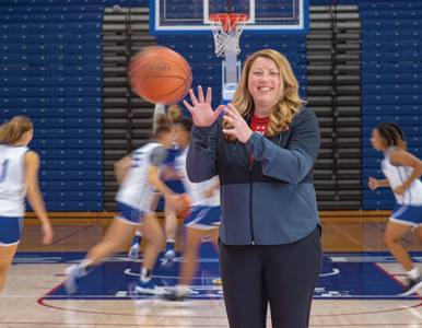 Tiffany Coll catches a basketball while basketball players run in the background