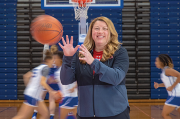 Tiffany Coll catches a basketball while basketball players run in the background