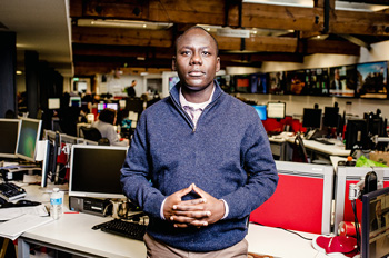 Derek Karikari stands at his desk at the AP newsroom in London