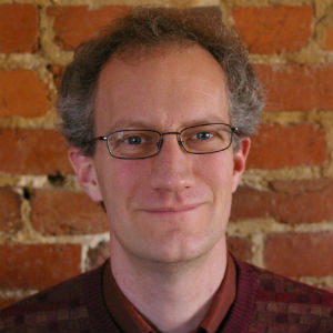 Person wearing glasses standing in front of brick wall