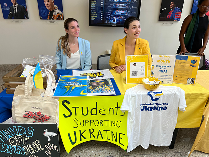 Anastasiia Baydyuk sits at a table with sign that says 