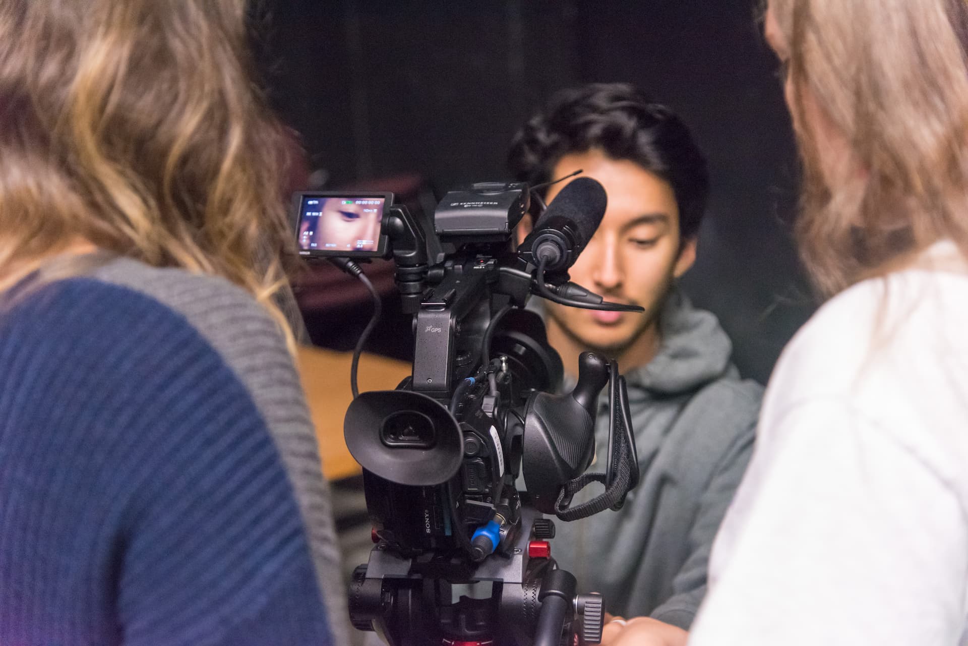 Three students stand near a camera in low lighting