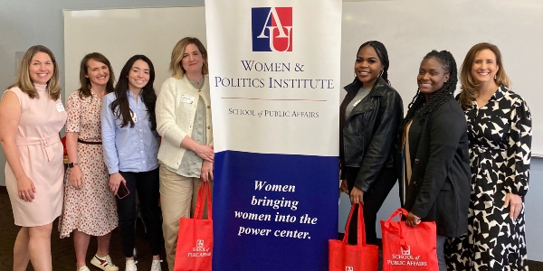 6 women of different races standing next to a banner