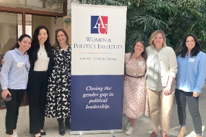 six women standing beside a banner