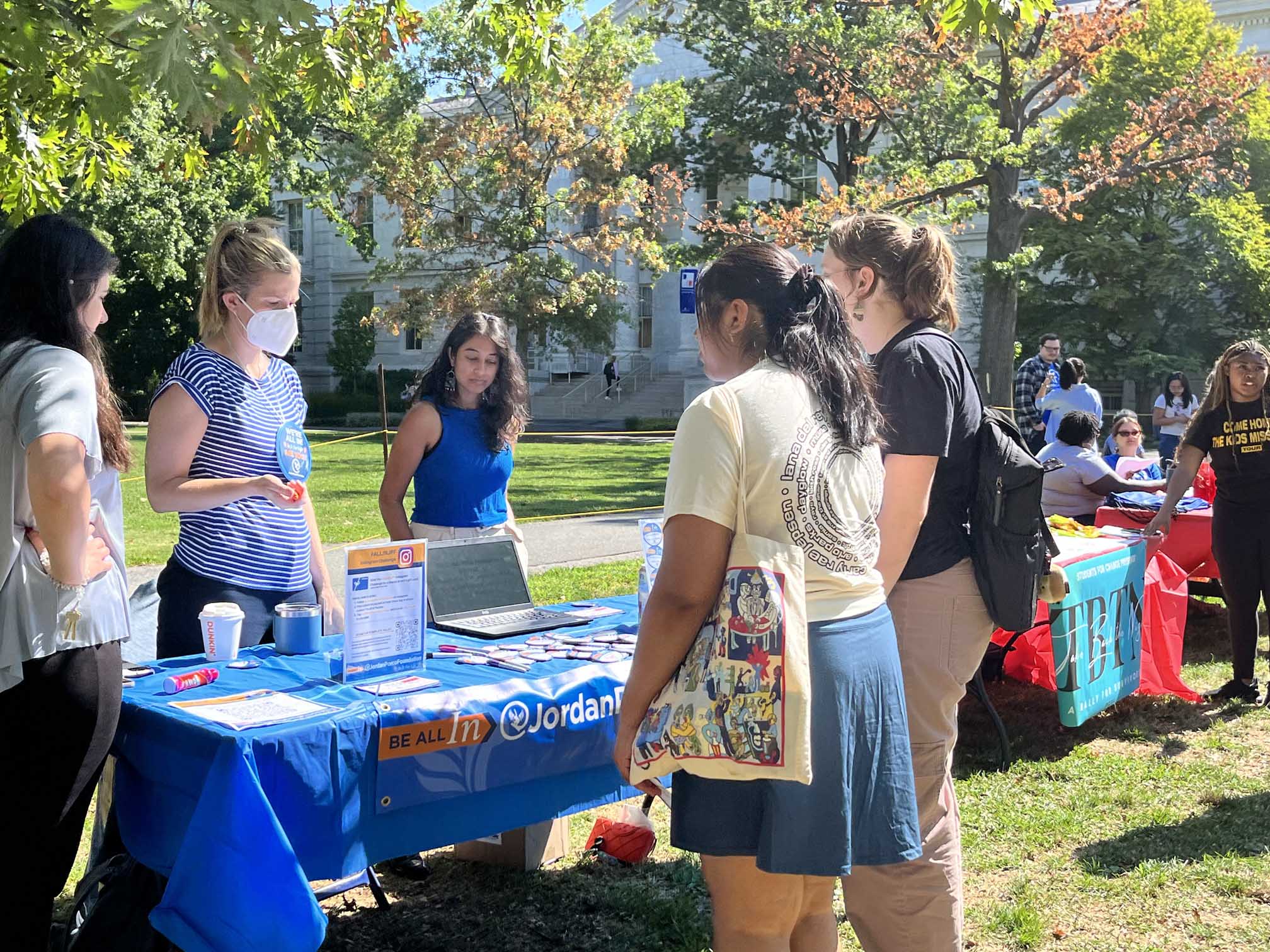 Two students stand in front of a table explaining Fresh Check Day, with three people standing by the table.