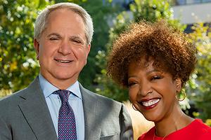 Man and woman smiling in front of trees.