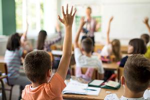 Children in classroom raising hands